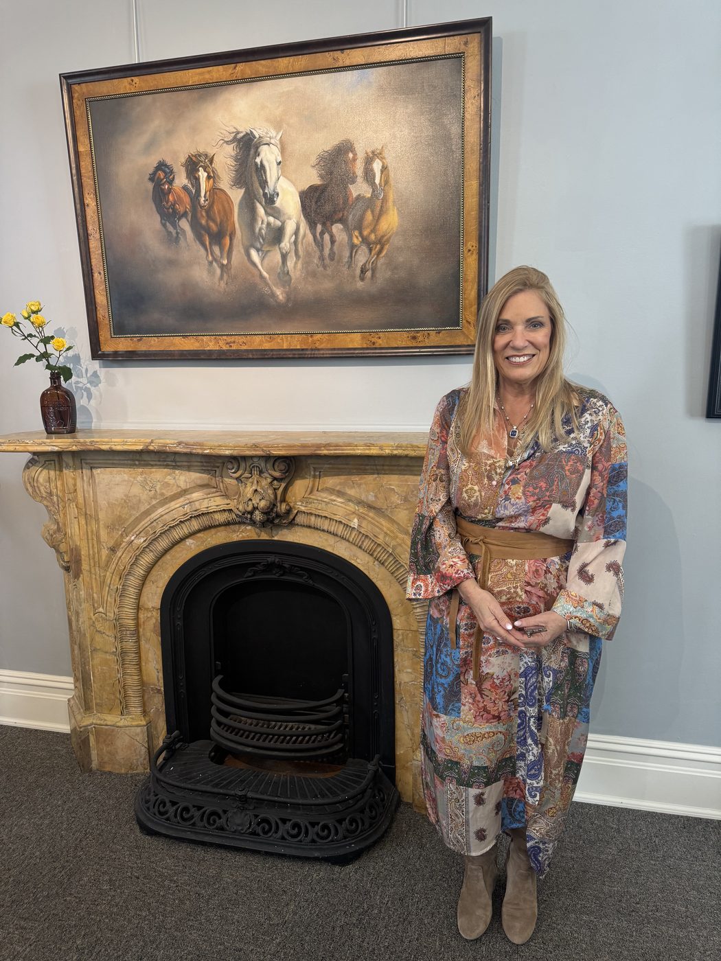 Dayna standing beside the running-horses painting hung above a marble mantel