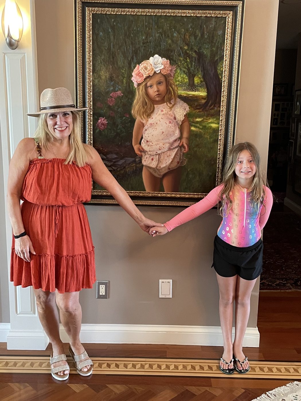 Dayna holding hands with a young girl beneath the flower-crown portrait