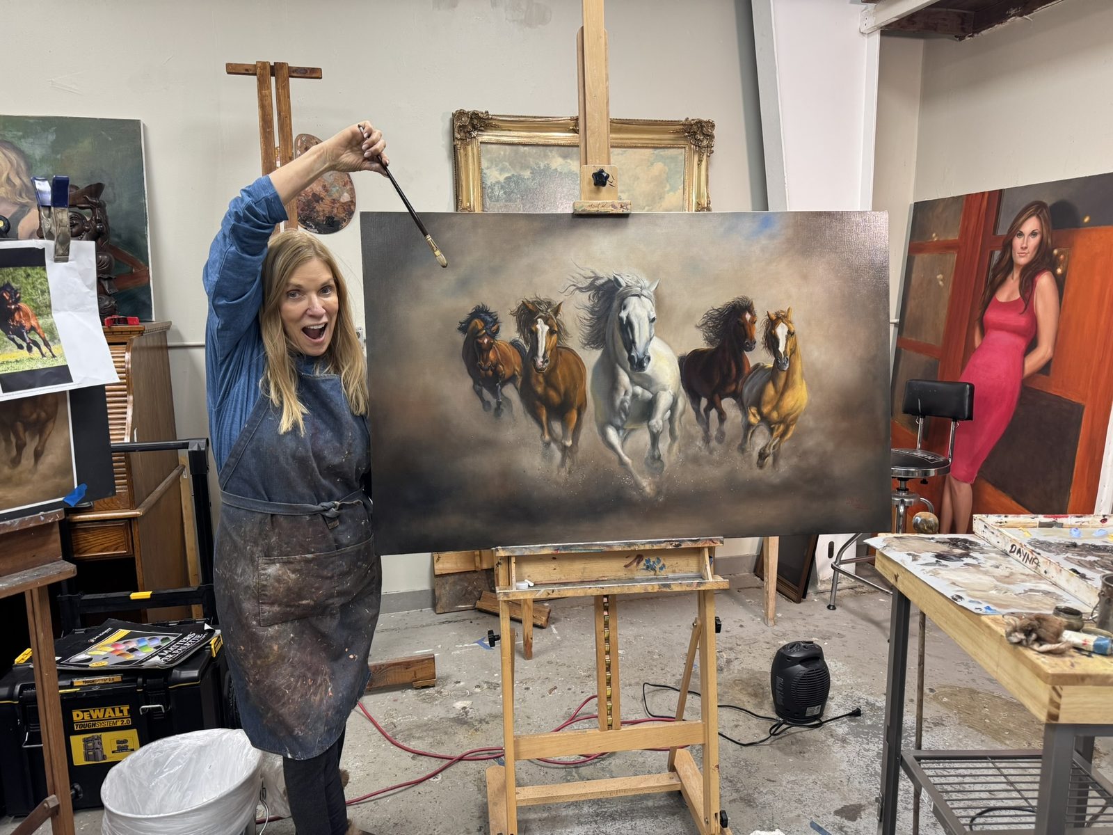 Dayna in her studio with the running-horses painting on the easel